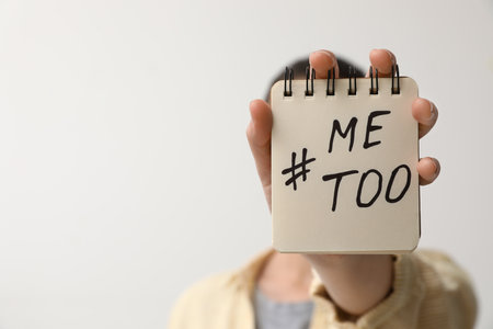 Woman holding notebook with hashtag MeToo against light background, closeup. Stop sexual assaultの写真素材