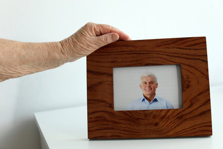Elderly woman with framed photo of her son indoors, closeupの写真素材