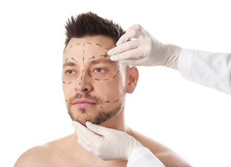 Doctor examining man's face before plastic surgery operation on white backgroundの写真素材