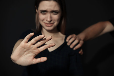 Man grabbing young woman with outstretched hand on dark background, closeup. Stop sexual assaultの写真素材
