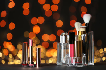 Bright lipsticks and holder with other makeup products on table against blurred lightsの写真素材