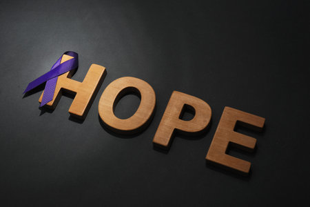 Purple awareness ribbon and word HOPE made of wooden letters on black backgroundの写真素材