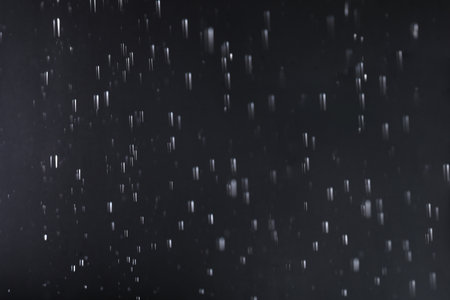 Rain drops falling down against dark backgroundの写真素材
