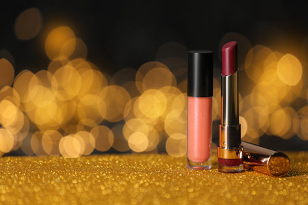 Bright lipsticks on table with gold glitter against blurred lights, space for textの写真素材