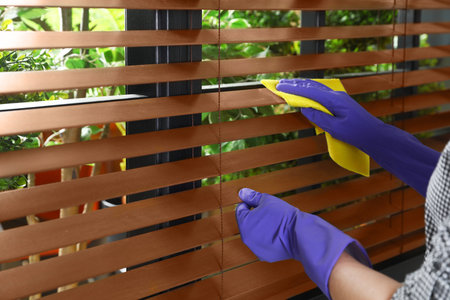 Janitor wiping window blinds with rag indoors, closeup. Space for text