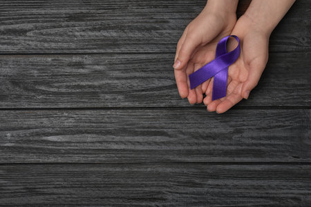 Woman holding purple awareness ribbon on black wooden background, top view with space for textの写真素材