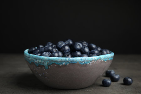 Bowl of tasty blueberries on gray table against black backgroundの写真素材