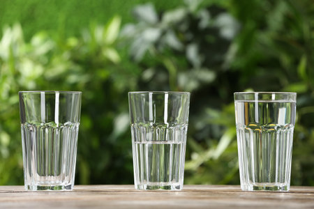 Empty, half and full glasses of water on wooden table against blurred backgroundの写真素材