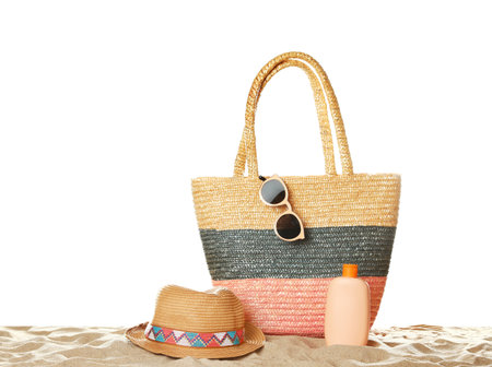 Wicker bag and beach accessories on sand against white background, space for textの写真素材