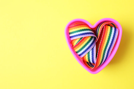 Heart shaped mold and bright rainbow ribbon on color background, top view with space for text. Symbol of gay communityの写真素材