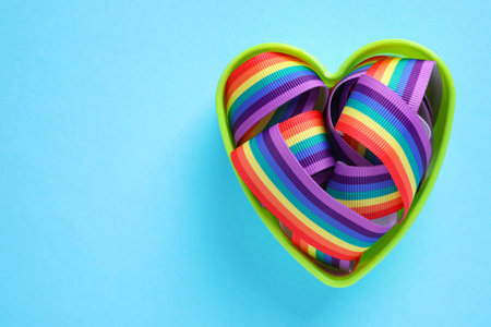 Heart shaped mold and bright rainbow ribbon on color background, top view with space for text. Symbol of gay communityの写真素材