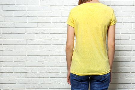 Back view of young woman wearing blank t-shirt near white brick wall, closeup. Mockup for designの写真素材