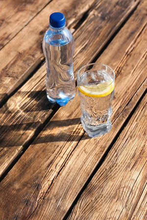 Glass and bottle of refreshing drink for hot summer day on wooden table, space for textの写真素材