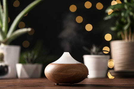 Composition with modern essential oil diffuser on wooden table against blurred lights, space for...