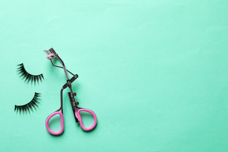 False eyelashes and curler on turquoise background, flat lay. Space for text