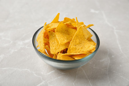 Tasty mexican nachos chips in glass bowl on gray table