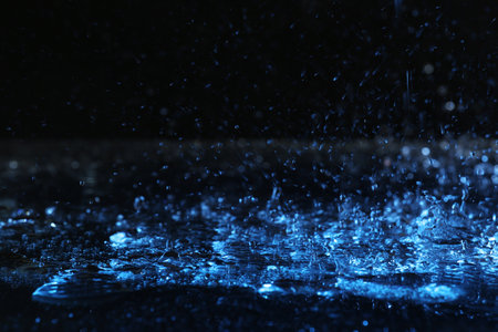 Heavy rain falling down on ground against dark background, toned in blueの写真素材