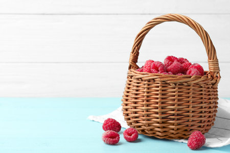 Basket of delicious fresh ripe raspberries on blue wooden table against white background, space for textの写真素材