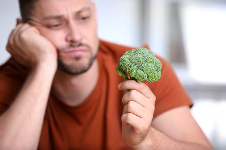 Unhappy man with broccoli on light background, closeupの写真素材