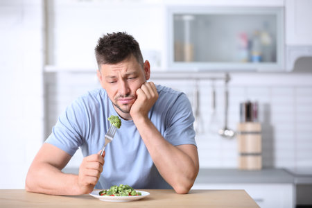 Portrait of unhappy man eating broccoli salad in kitchenの写真素材