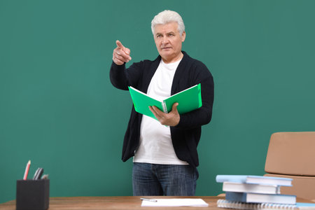 Portrait of senior teacher with notebook at green chalkboard and tableの写真素材
