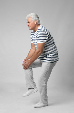 Full length portrait of senior man having knee problems on grey backgroundの写真素材