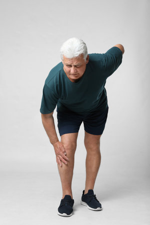 Full length portrait of senior man having knee problems on grey backgroundの写真素材