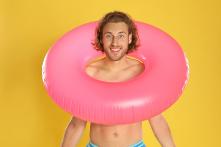 Attractive young man in swimwear with pink inflatable ring on yellow backgroundの写真素材