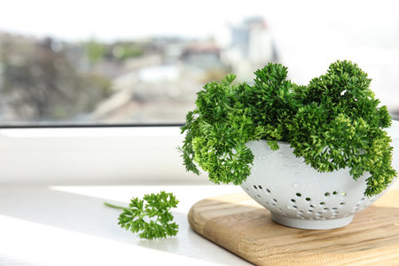 Colander with fresh green parsley on window sill indoors, space for textの写真素材