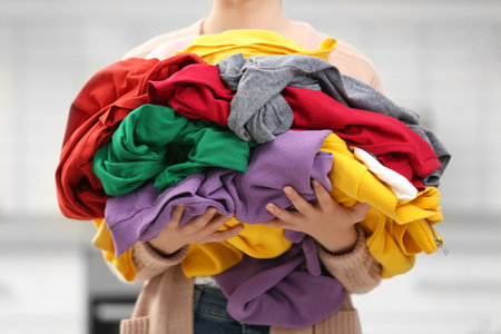 Woman holding pile of dirty laundry indoors, closeupの写真素材