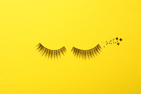 False eyelashes and sparkles on yellow background, flat layの写真素材
