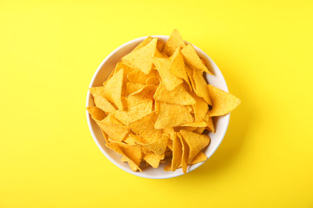Tasty mexican nachos chips in bowl on yellow background, top viewの写真素材