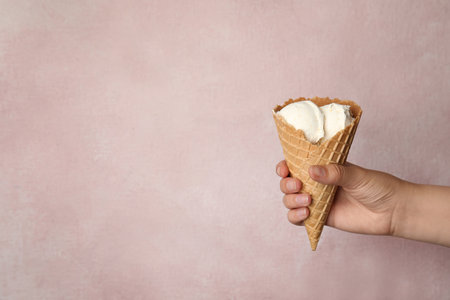 Woman holding delicious ice cream in wafer cone on pink background, closeup. Space for text