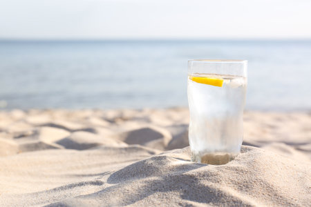 Sandy beach with glass of refreshing lemon drink on hot summer day, space for textの写真素材