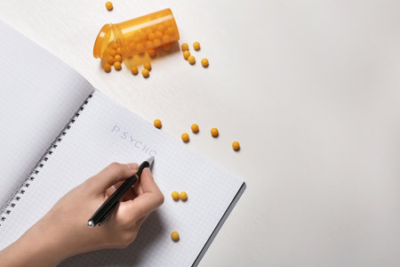 Woman writing word PSYCHO in notebook near jar of pills on table, closeup. Space for textの写真素材