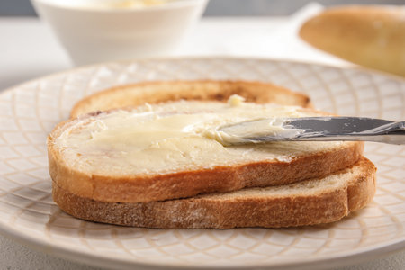 Spreading tasty butter onto slice of bread with knife on plate, closeupの写真素材