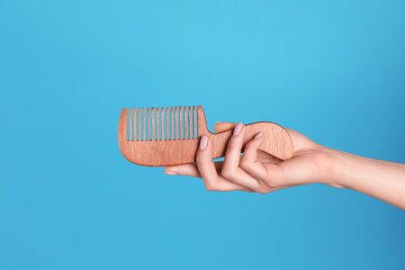 Woman holding wooden hair comb against blue background, closeupの写真素材