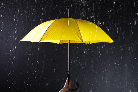 Woman holding bright umbrella under rain on dark background, closeupの写真素材