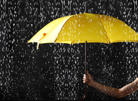 Woman holding bright umbrella under rain on dark background, closeupの写真素材