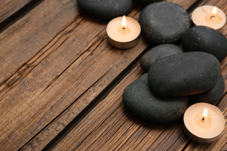 Spa stones and lit candles on wooden background, space for textの写真素材