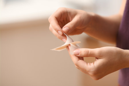 Woman unpacking medical patch against blurred background, closeup. Space for textの写真素材