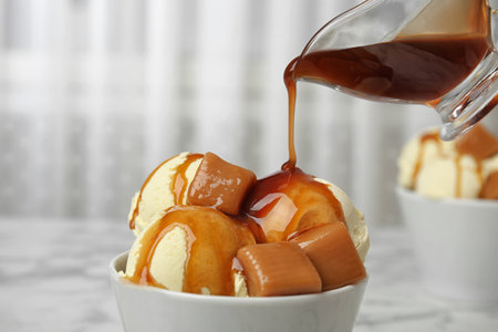 Pouring caramel sauce onto delicious ice cream in bowl on table, closeup. Space for textの写真素材