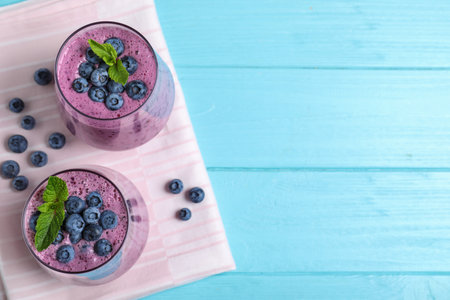 Glasses of tasty blueberry smoothie and fabric on light blue wooden table, flat lay. Space for textの写真素材