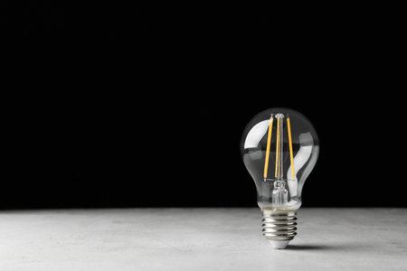 Vintage lamp bulb on light table against black background. Space for textの写真素材
