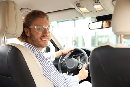 Attractive young man driving his luxury car, view from backseat
