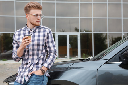 Attractive young man with cup of coffee near luxury car outdoorsの写真素材