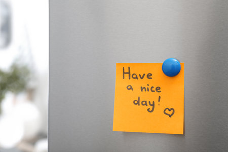 Note with text "Have a nice day" and magnet on refrigerator door in kitchen. Space for textの写真素材