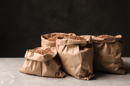 Paper bags with uncooked buckwheat on gray marble table against black background. Space for textの写真素材