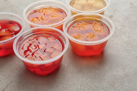 Plastic containers with tasty jelly desserts on gray table