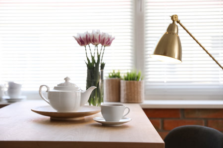 Tea set on table near window with blinds indoorsの写真素材
